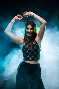 Neşeli bir gece kulübünde dans eden gülümseyen kadın renkli ışık ve duman efektleriyle, mutluluk ve heyecanı ifade ediyor..