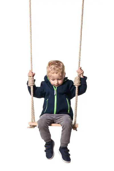 Stock image Cute little boy in blue jacket and grey pants sitting on a swing, isolated on white background.