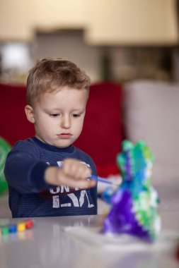 Mavi süveter giyen küçük bir çocuk, çocukluğunu ve hayal gücünü gözler önüne seren cam bir masada canlı, çok renkli bir dinozor oyuncağıyla oynarken derinden konsantre olur..