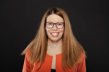 Gözlük takan neşeli profesyonel bir kadının portresi ve parlak turuncu bir bluz koyu bir arka planda duruyor, kendine güven ve pozitiflik yayıyor..