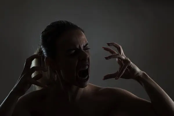 stock image A moody and intense image capturing a young woman with an expression of extreme fear or anger. The dim lighting highlights her dramatic gestures and facial expression.