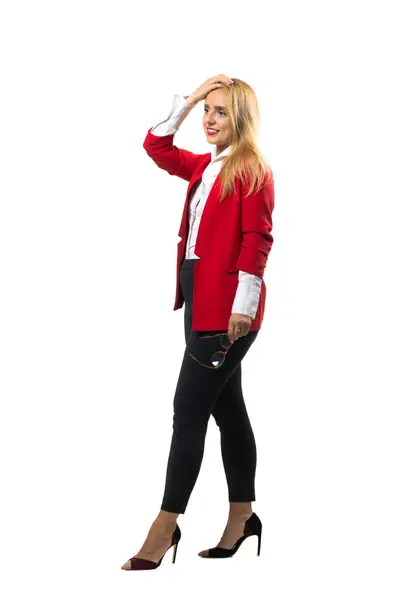 stock image An elegant business woman smiles confidently, wearing a red blazer and white shirt while holding glasses in a professional setting.