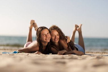 Kumsalda uzanan iki mutlu arkadaş, deniz kenarında güneşli bir yaz gününün tadını çıkarıyorlar. Tatil titreşimleri ve arkadaşlık.