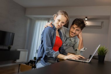 Genç bir adam ve kadın birlikte duruyorlar, parlak, çağdaş dairelerinde dizüstü bilgisayar kullanıyorlar, takım çalışmalarını ve bağlantılarını gösteriyorlar..
