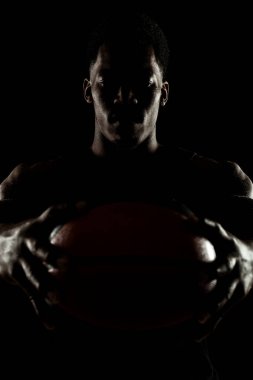 Basketball player holding a ball against black background. Serious concentrated african american man. Muscular person sidelit silhouette. clipart