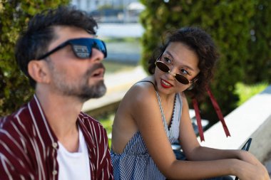 İki arkadaş parkta otururlar, şık güneş gözlüğü takarlar, güneşli bir günde sıradan bir sohbete girerler..