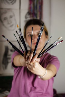 Artistic girl holding many dirty colorful used brushes with both hands. clipart