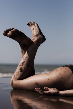 Rahatlatıcı bir plaj sahnesi, kumlu bacakları ve ayakları açık gökyüzüne karşı neşeyle yükselen bir kadını gösteriyor..