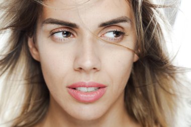 Bu resim, saçları rüzgarla dağılmış, düşünceli bir ifade ve doğal bir güzelliğe sahip genç bir kadının yakın plan portresini çekiyor..