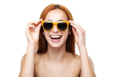 Neşeli, genç, kızıl saçlı bir kadın neşeli bir anın tadını çıkarıyor. Havalı turuncu güneş gözlükleri takıyor ve parlak beyaz bir gülümseme sergiliyor..