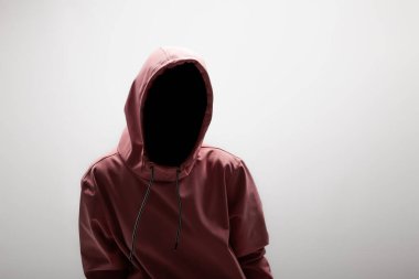 Gizemli ve modern: pembe kapüşonlu genç bir kadın, yüzü belirsiz, yumuşak gri bir arka plana karşı poz veriyor..