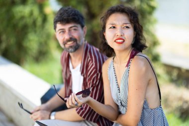 Açık havada güneşli bir günün tadını çıkaran, parkta oturup gülümseyen bir kadın ve erkeğin samimi bir fotoğrafı..