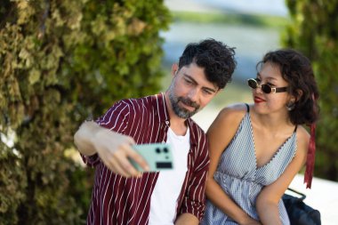 Bir erkek ve kadın açık havada güneşli bir günün tadını çıkarırlar, birlikte selfie çekerler ve dostluk ve rahatlama anlarını kucaklarlar..