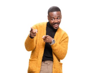 Hardallı bir süveter giyen neşeli bir adam parlak bir stüdyo arkaplanına gülümsüyor, sıcaklığını ve pozitifliğini iletiyor..