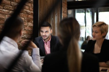 Bir grup genç profesyonel, modern bir kafede, takım çalışması ve işbirliği sergileyerek ciddi bir iş görüşmesine giriştiler..