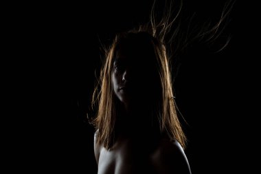 A striking image capturing a young woman's profile with her hair dramatically blowing in the wind, set against a black background under moody lighting. clipart