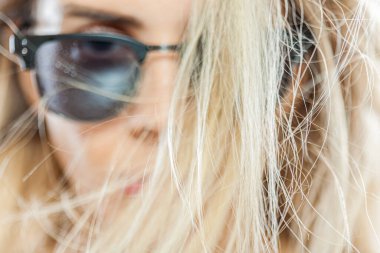 Bu görüntü, güneş gözlüğü takan, sarı saçlı, rüzgarın savurduğu şık bir kadının yakın plan görüntüsünü yakalıyor..