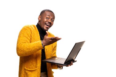 Sarı kazaklı neşeli bir adam dizüstü bilgisayar tutuyor ve hoş geldin jesti yapıyor. Parlak bir stüdyo ortamında arkadaşlığı ve teknolojiyi somutlaştırıyor..