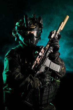 Gelişmiş taktik teçhizat ve gece görüşü teçhizatı takan bir asker dramatik yeşil bir duman geçmişine karşı bir tüfek tutuyor, otoriteyi somutlaştırıyor, hazır ve savaşıyor..