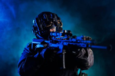 Gelişmiş teçhizat ve tüfekle donatılmış bir asker, dramatik bir karamsar arka planda, askeri hazırlık ve odaklanma tasvir ediyor..