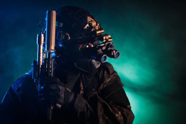 Dramatik ışıklandırma altında dumanlı bir atmosferde modern taktik teçhizat ve silahlarla donatılmış bir asker..