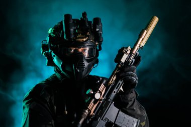 İleri taktik teçhizatlı bir asker dramatik dumanlı bir arka plana karşı tüfek tutuyor. Güvenlik, askeri operasyonlar, taktik uzmanlık, koruma ve savaşa hazırlık kavramları için idealdir..