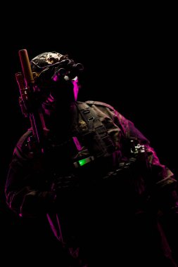 Muharebe teçhizatı takan ve karanlık bir ortamda gece görüş gözlüğü takan bir taktik operatörü askeri hazırlığı görsel olarak çarpıcı bir şekilde canlandırıyor..