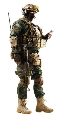 Tam teçhizatlı silahlı bir asker, gelişmiş askeri teçhizat ve hazırlık gösteren el bilgisayarı inceliyor. Görüntü modern savaş teknolojileri ve profesyonelliği vurguluyor.