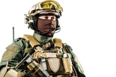 Gelişmiş taktik teçhizatla donatılmış, çelik yelek, miğfer ve iletişim cihazı takan modern asker dikkatli bir şekilde ayakta duruyor. Çarpıcı bir görüntüde askerlik hizmeti, operasyona hazırlık ve güvenlik kavramlarını yakalar.