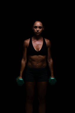 Siyah spor kıyafetleriyle spor yapan sporcu, yeşil halterlerle dramatik bir şekilde aydınlatılmış bir stüdyoda fiziksel güç ve kararlılık sergiliyor..