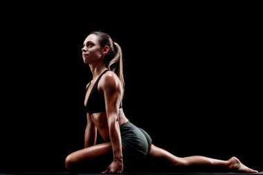 Formda bir kadın yoga seansına katılır, gücünü gösterir ve keskin siyah bir zemine karşı duruşuna odaklanır.