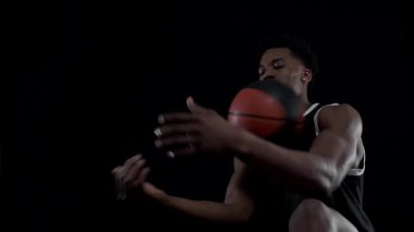 Basketbolcu topu dengeliyor. Siyah arka planda oturan ve pratik yapan Afrikalı Amerikalı sporcu