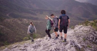 Dağlarda kayalık bir patikada yürüyüş yapan bir grup arkadaş. Çevreleri yemyeşil ormanlarla ve güzel bir göl manzarasıyla çevrili. Doğanın neşesini yaşıyorlar..