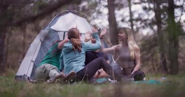 Bir grup arkadaş çadırlarının dışında bir ormanda kamp gezisinin tadını çıkarıyor ve beşlik çakarak kutluyorlar. Bir açık hava gezisi sırasında neşe ve macera anları yakalıyorum..