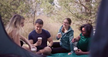 Bir grup arkadaş çadırın dışında birlikte oturup, ormanda yürüyüş yaparken kahve molası veriyorlar, kahkahalar ve hikayeler anlatıyorlar..