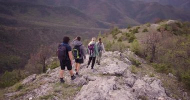 Dağlarda kayalık bir patikada yürüyüş yapan bir grup arkadaş. Çevreleri yemyeşil ormanlarla ve güzel bir göl manzarasıyla çevrili. Doğanın neşesini yaşıyorlar..