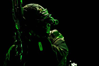 Çarpıcı yeşil bir siluette gece görüş teknolojisiyle donatılmış ağır silahlı bir operatör, izole edilmiş siyah, gizemli bir şekilde taktiksel hazırlık ve modern askeri teçhizatı sembolize ediyor.