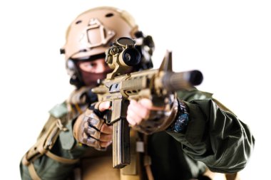 İleri askeri giyimli bir taktik asker tüfeği odaklanmış olarak hedefliyor. Bulanık arka plan, bu hassas ve yoğun anda iletilen eylem ve disiplini yoğunlaştırır..