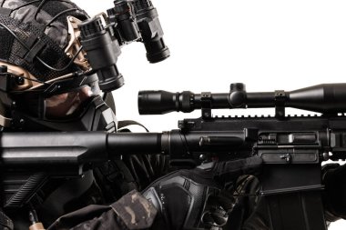 Tüfek ve gece görüş gözlüğü de dahil olmak üzere taktik teçhizatlı bir asker dikkatle yaklaşır. Kurulumda taktik operasyonlar veya eğitim alanındaki hassasiyet, hazırlık ve askeri uzmanlık vurgulanıyor