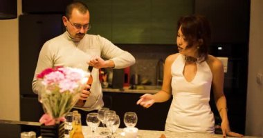 Romantik bir akşam için hazırlanan bir çift modern mutfaklarında kadehlere gül şarabı döküyor. Sıcak ışıklar ve çiçekler samimi bir ortam hazırlar..