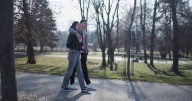 Genç bir çift güneşli bir günde parkta yürüyor, birbirlerine eşlik etmekten ve güzel manzaradan keyif alıyorlar..