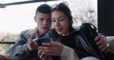 Genç bir çift birlikte oturuyor, sosyal medyada geziniyor ya da akıllı telefon kullanarak internetten alışveriş yapıyor. Mutlu ve meşgul görünüyorlar..