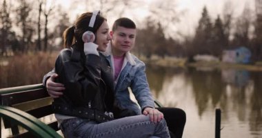 Genç çift gölün kenarındaki bankta müzik dinlemekten hoşlanıyor. Kulaklıkları, romantizmi ve deniz kıyısındaki bağlantıları paylaşıyoruz..