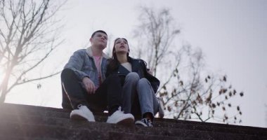 Genç bir çift basamaklara oturur, geleceği hayal ederken işaret eder ve konuşurlar..