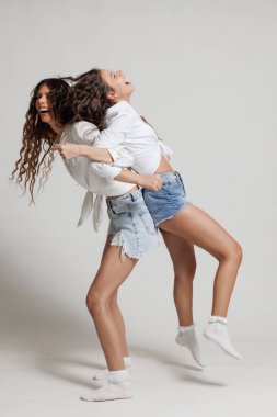 Parlak bir stüdyo ortamında kot şort ve günlük gömlekler giyerken gülüp eğlenen iki genç kadın.