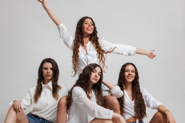 Neşeli ve şık bir kompozisyonda poz veren günlük beyaz gömlekli ve kot şortlu dört kadın. Görüntü, arkadaşlık, neşe, birlik, yoldaşlık ve özgüven gibi kavramları tasvir eder..