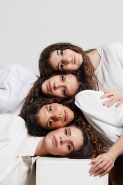 Süslü beyaz kıyafetlerle birbirine kafa tutan dört kadının grup portresi, minimalist ve zarif bir kompozisyonda dostluğu, güveni ve birliği simgeliyor..