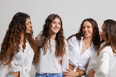 Dört genç kadın bir arada duruyor ve gülüşmelerini paylaşıyor, arkadaşlıklarını ve neşelerini ifade ediyorlar. Açık bluz ve kot pantolon giyiyorlar, pozitif enerji ve gençlik enerjisi yayıyorlar..