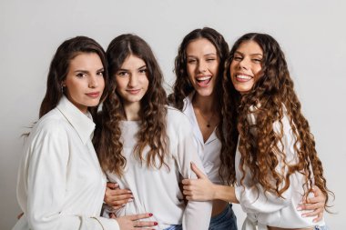 Beyaz gömlekler giymiş, gülümseyen ve stüdyo ortamında eğlenen bir grup neşeli genç kadın. Atmosfer neşe, dostluk ve pozitiflikle dolu..