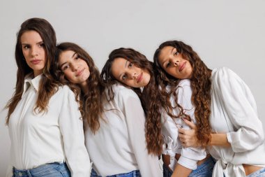 Beyaz gömlekli dört gülümseyen kadın birlikte poz veriyor, dostluk, neşe ve birlik gösteriyorlar. Görüntü, bir arkadaş grubunu arkadaşlıkla dolu rahat bir anın tadını çıkarırken resmediyor.